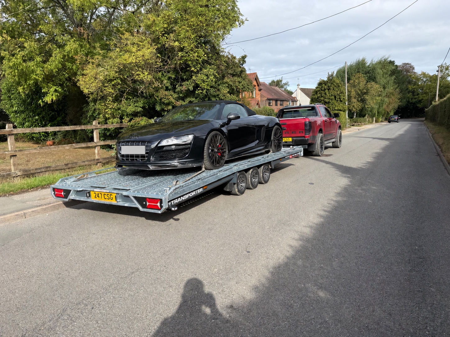 Black Audi secured on a vehicle transport trailer behind a red CSG pickup