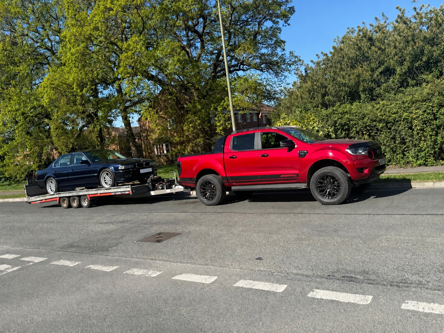 Blue BMW saloon secured on a trailer behind a red CSG pickup