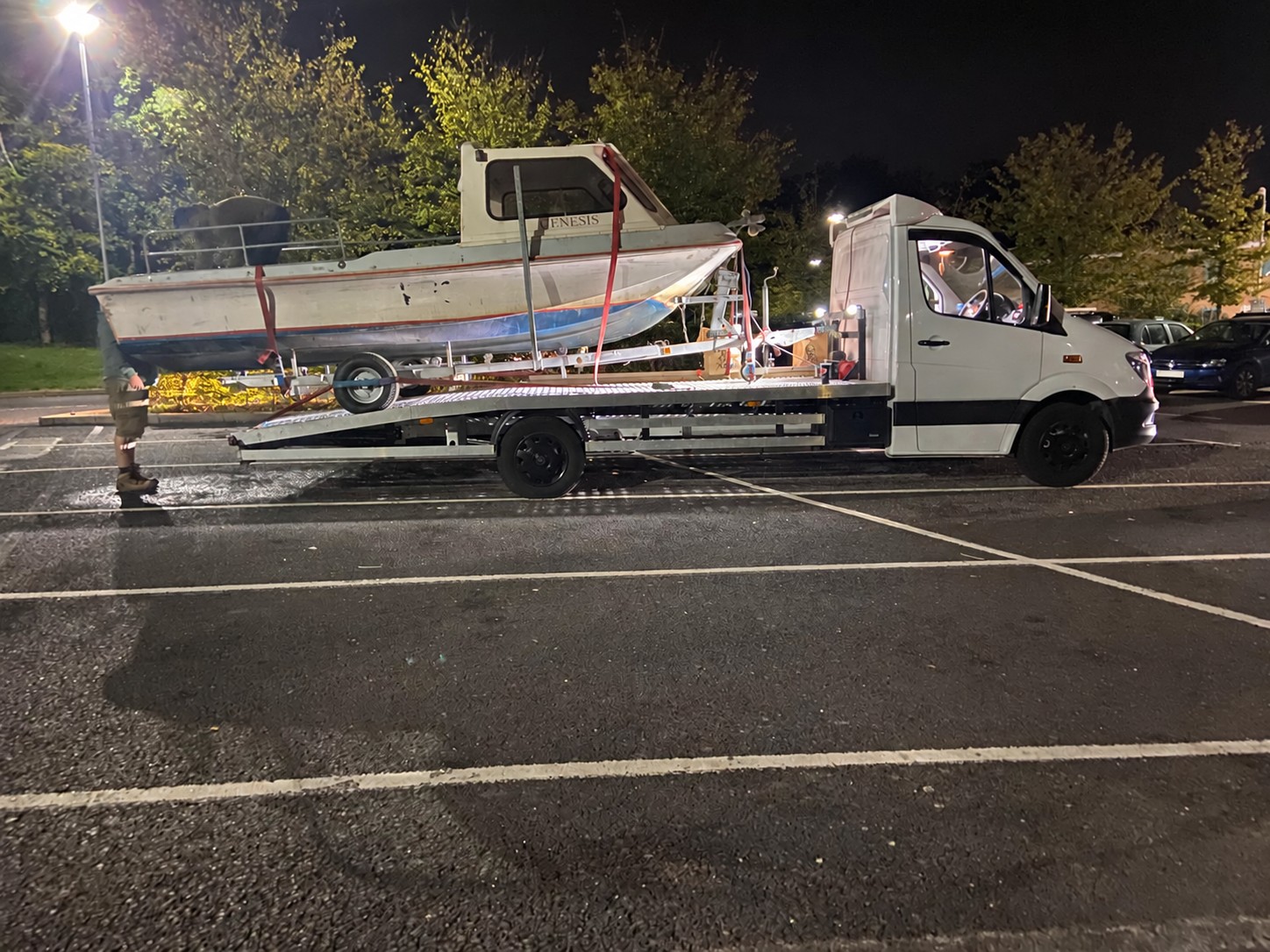 Boat secured on a white vehicle transporter at night