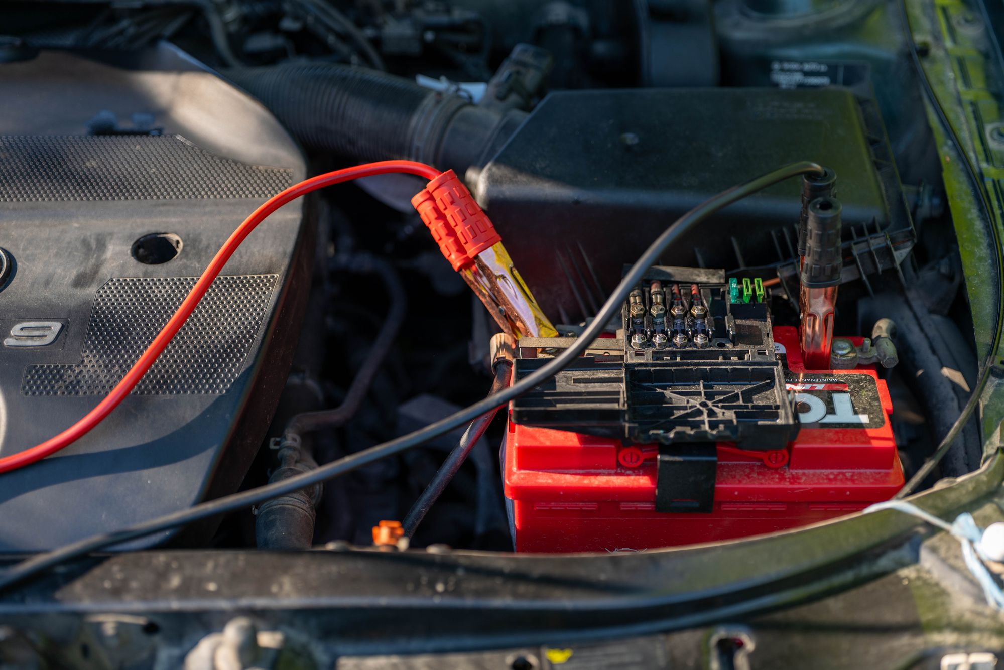 Red and black jump leads connected to a car battery