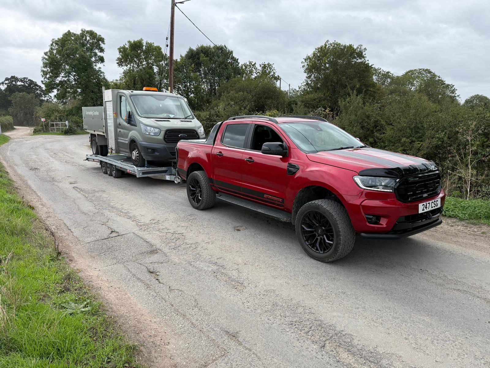 Red CSG Recovery pickup towing a trailer carrying a grey tipper van