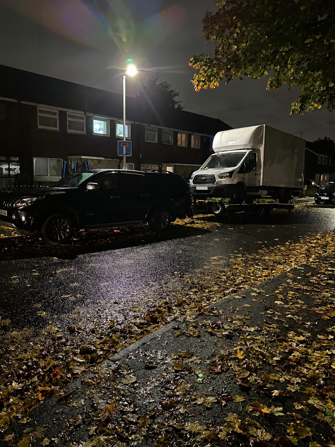 CSG pickup transporting a white box van on a trailer on a wet autumn night