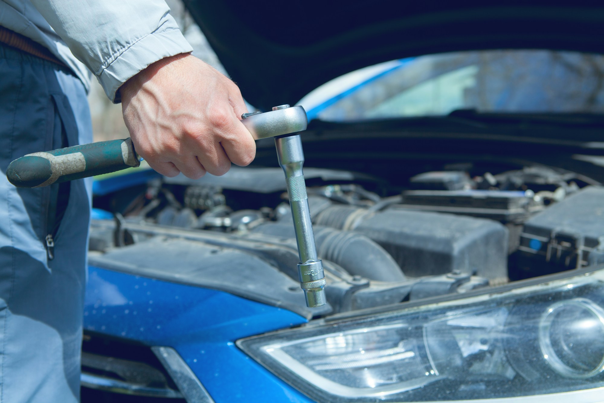 Mechanic holding a socket wrench beside an open car engine bay