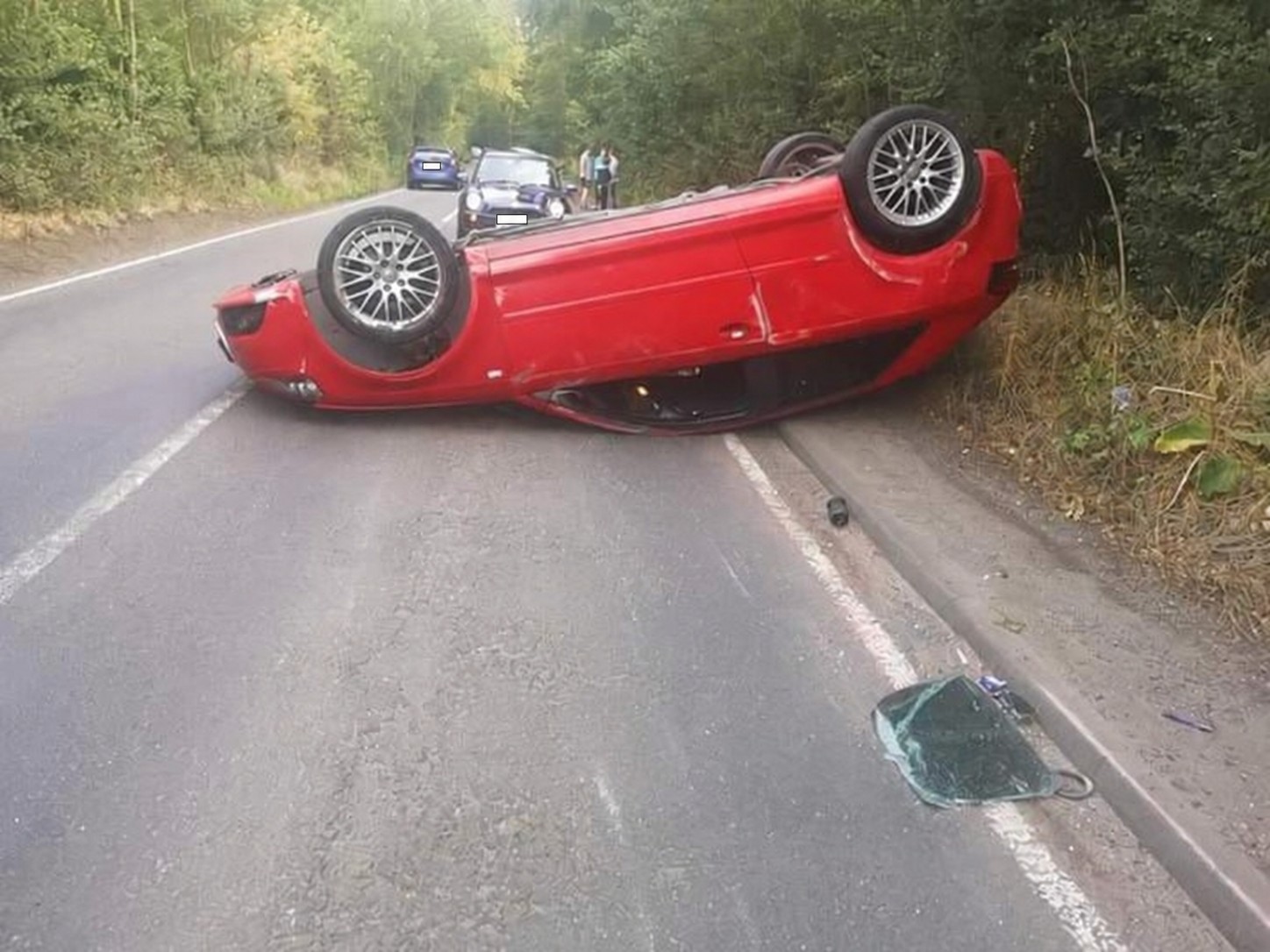 Overturned red car on a rural road before recovery
