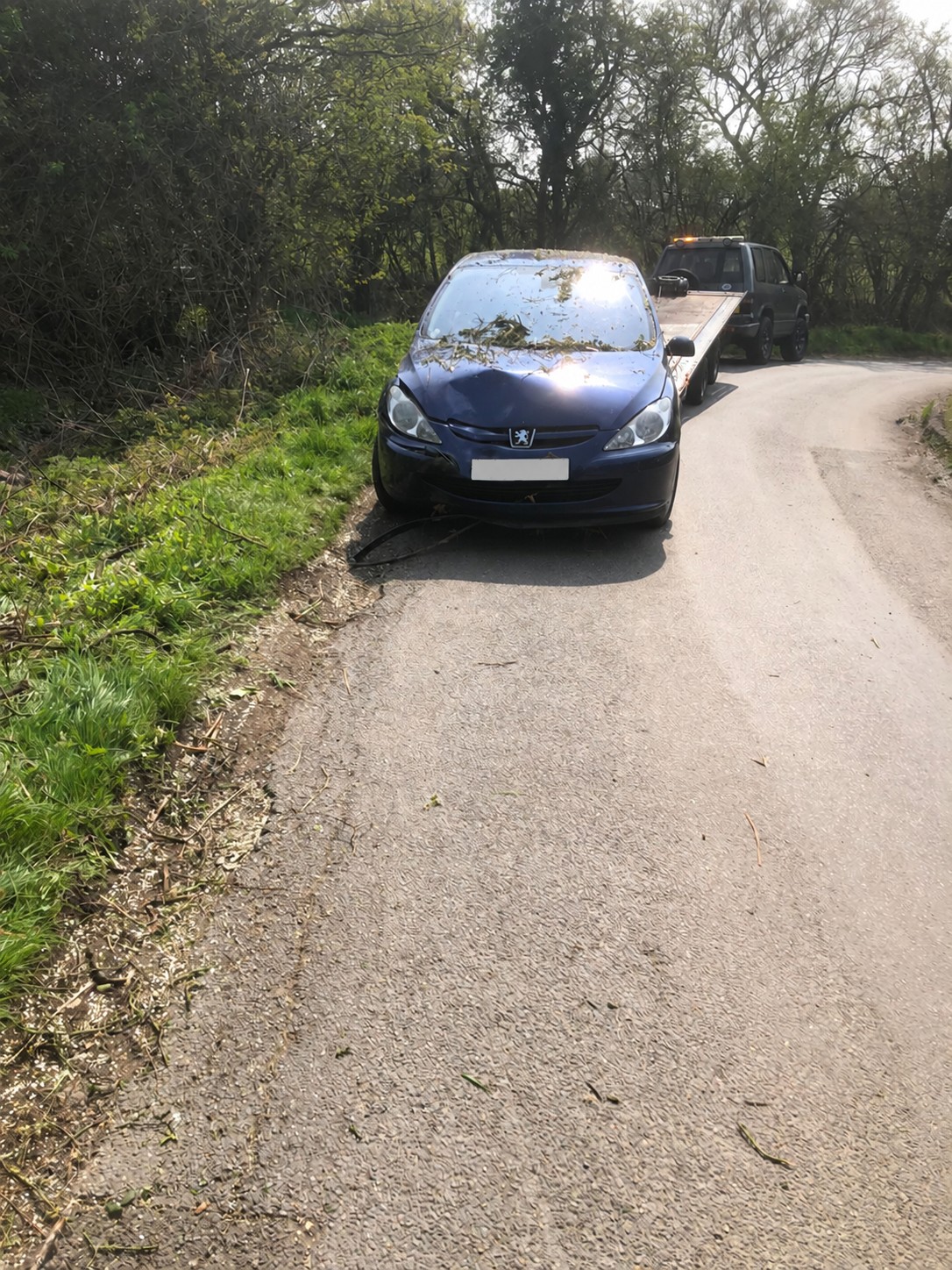 Blue Peugeot beside a lowered recovery ramp on a country lane