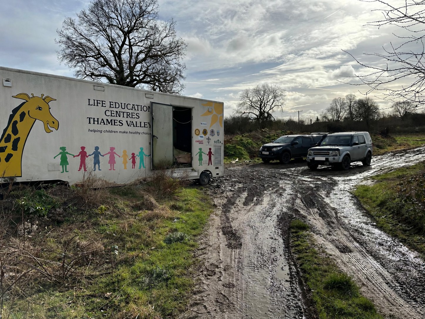 Recovery vehicles beside a mobile education trailer on a muddy track