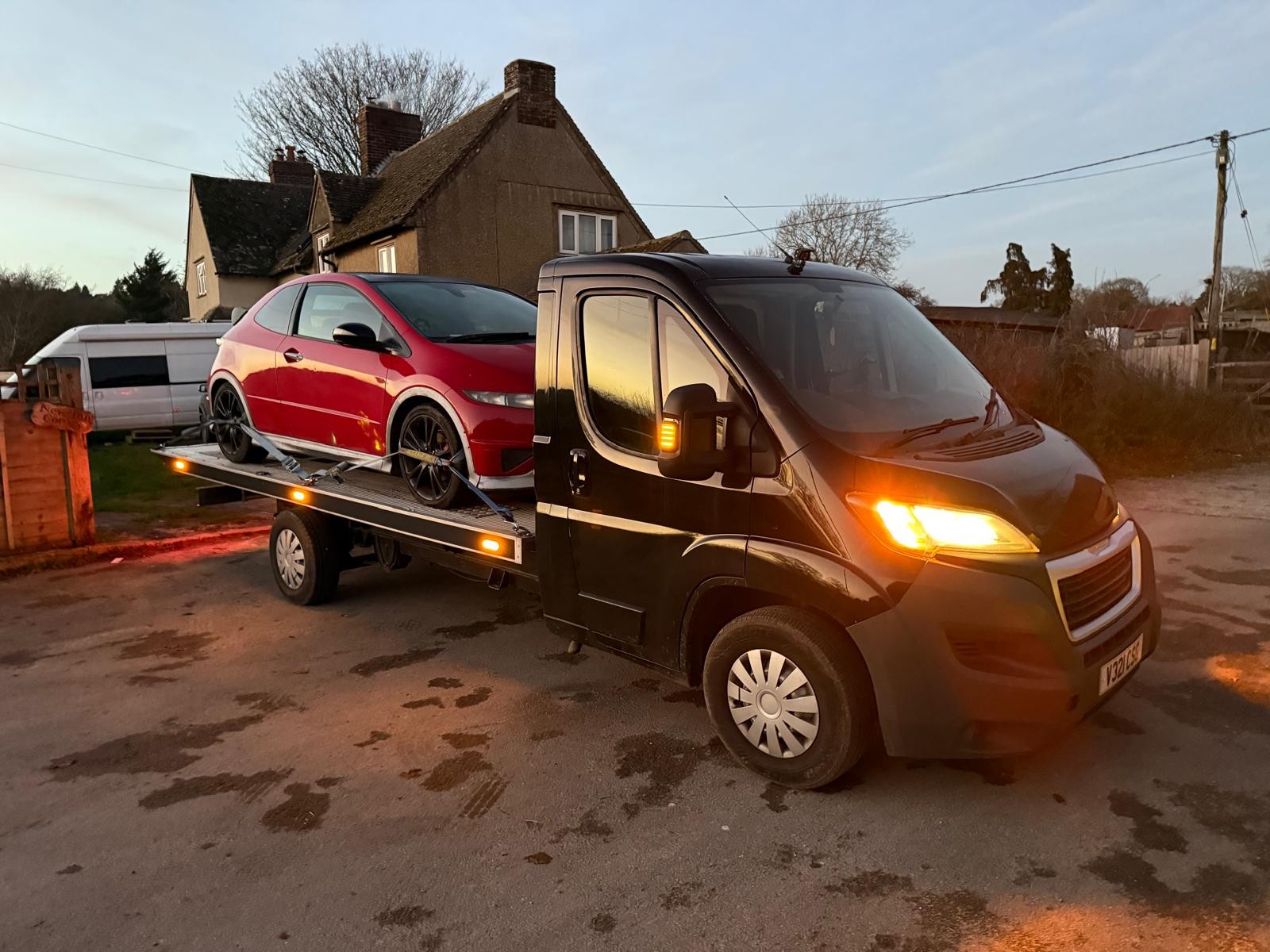 Red hatchback on the bed of a black CSG recovery truck at dusk