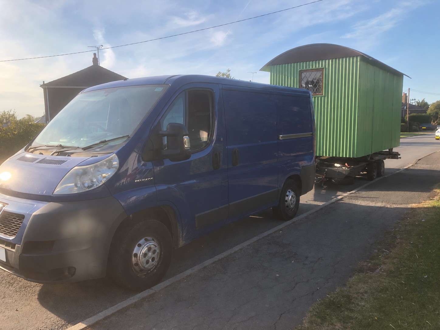 Blue van towing a green shepherd’s hut on a trailer