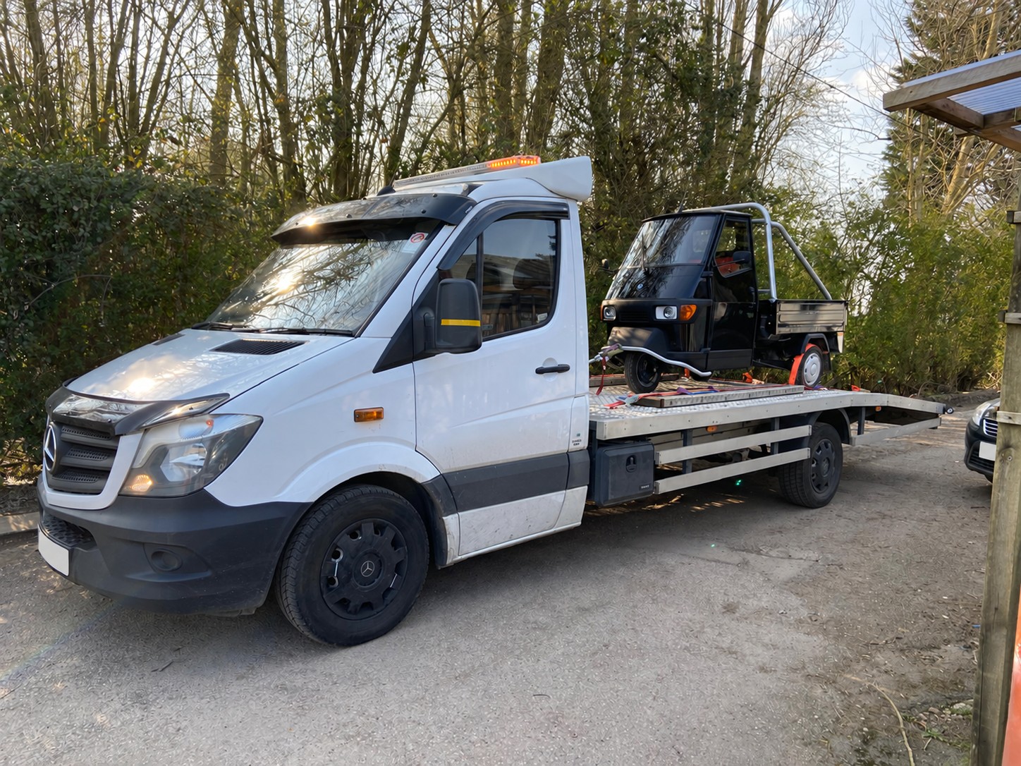 Small three-wheel utility truck secured on a white flatbed transporter