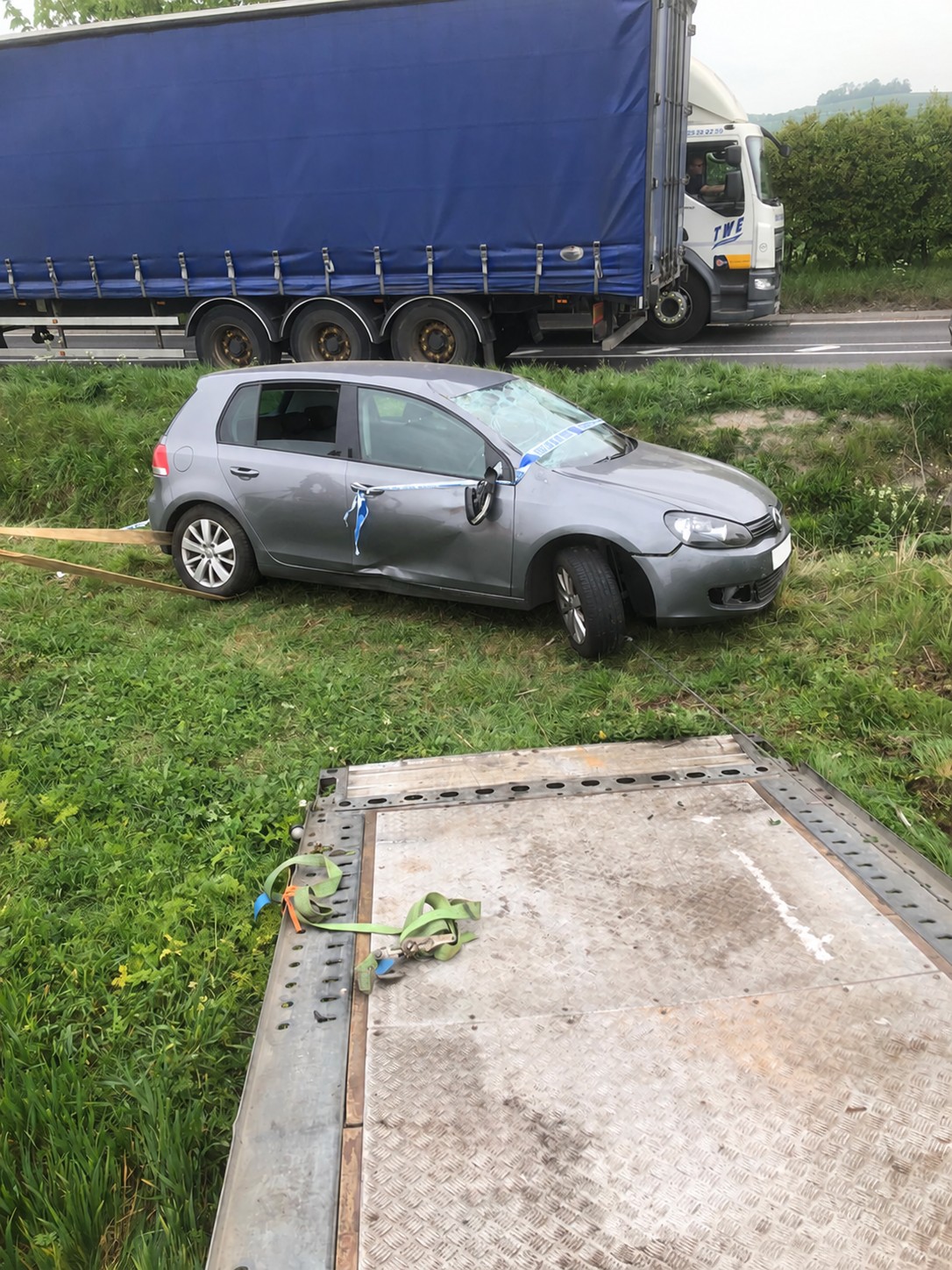 Damaged grey Volkswagen Golf in a roadside ditch beside a recovery ramp