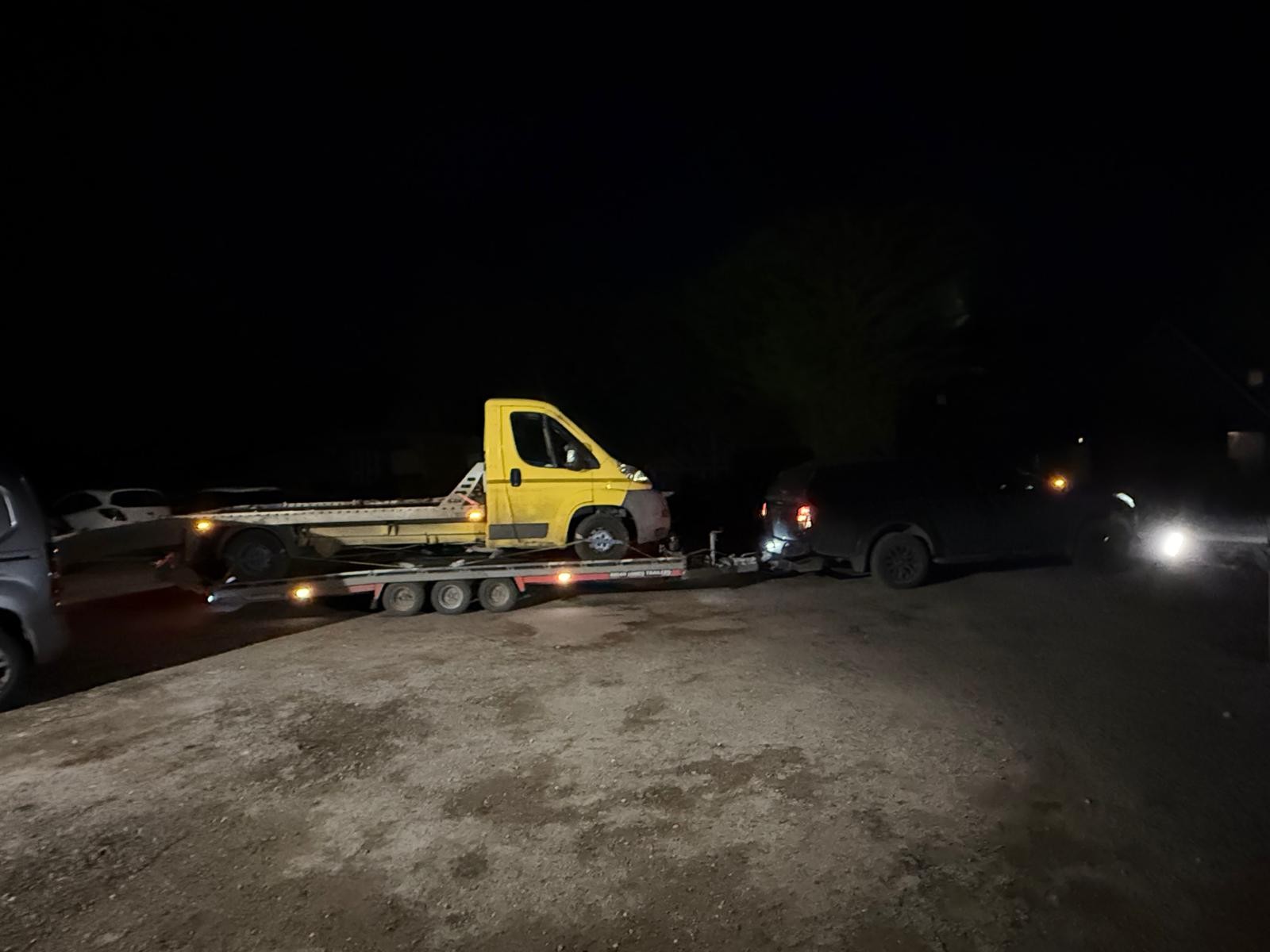 Side view of a yellow recovery truck carried on a CSG trailer at night